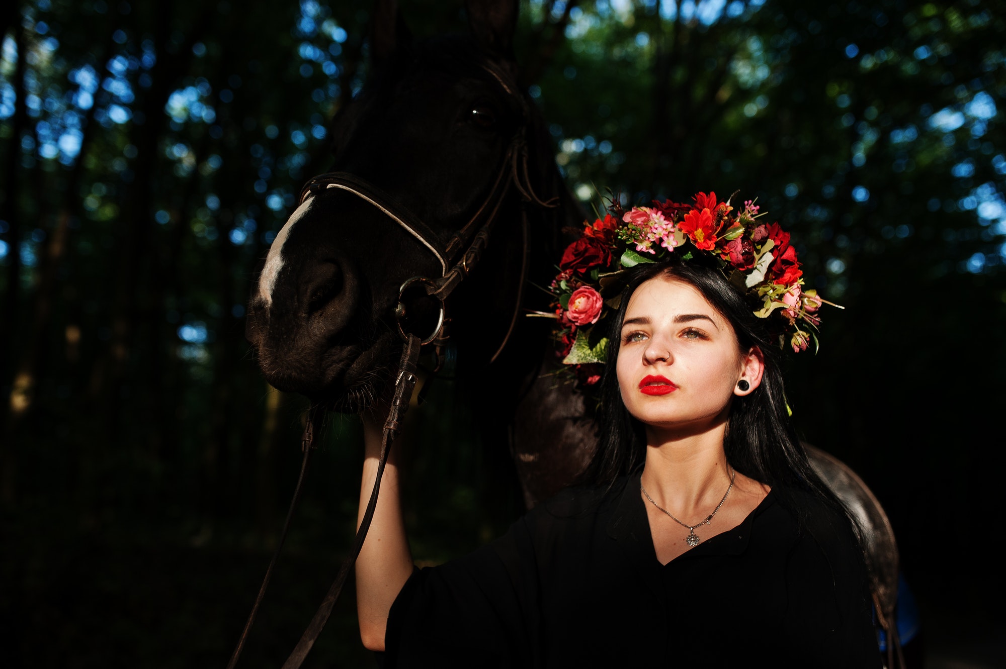 mystical girl in wreath wear in black with horse in wood